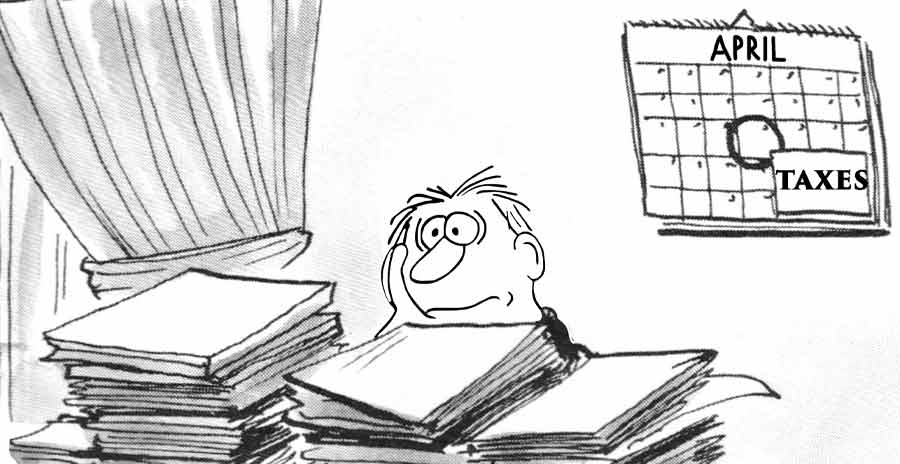 A stressed man sites behinds his desk, facing piles of paperwork on tax day.