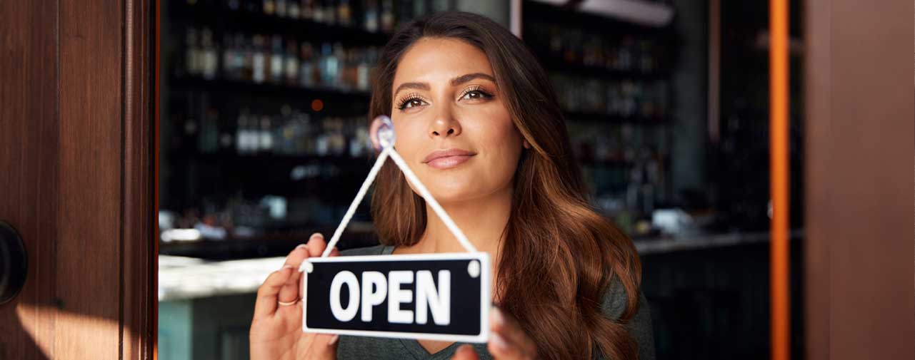 A female business owner flips the sign on her shop to "Open"